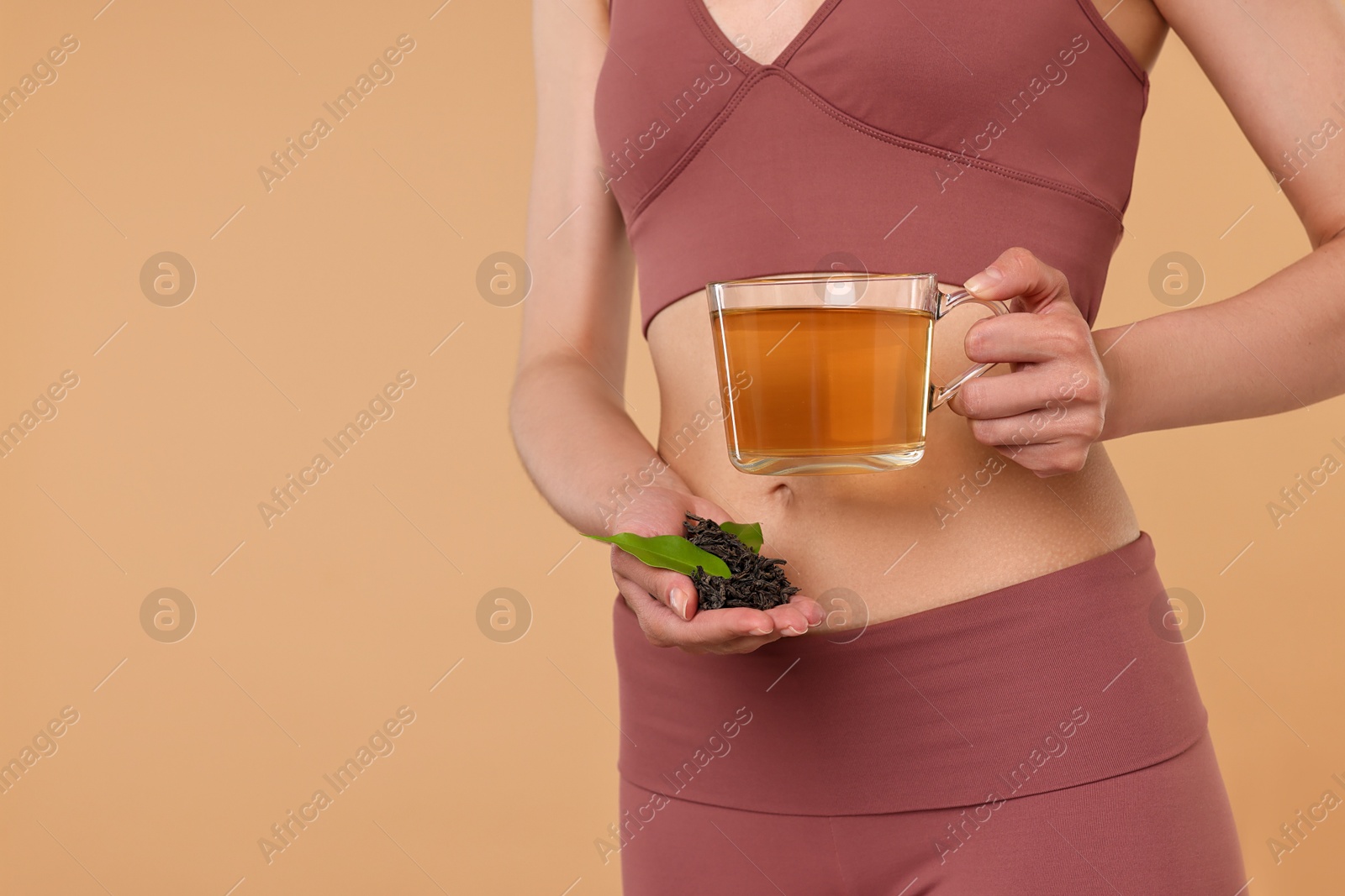 Photo of Weight loss concept. Woman with cup of diet tea and dry leaves on beige background, closeup