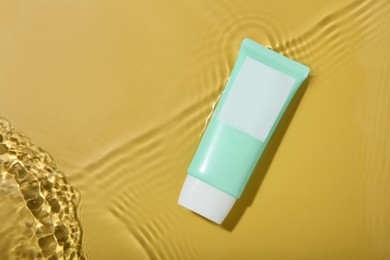 Photo of Tube with cream in water on yellow background, top view. Cosmetic product