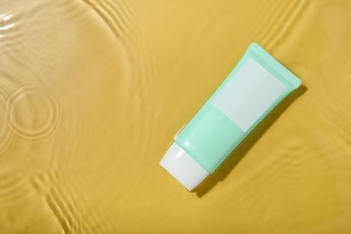 Photo of Cosmetic product. Tube with cream in water on yellow background, top view. Space for text