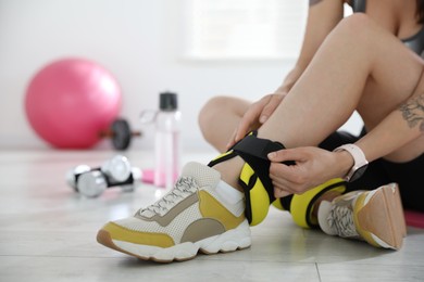 Woman putting on ankle weights indoors, closeup