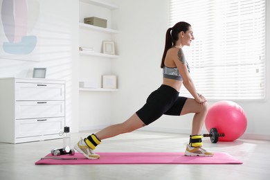 Beautiful woman with ankle weights doing exercises indoors