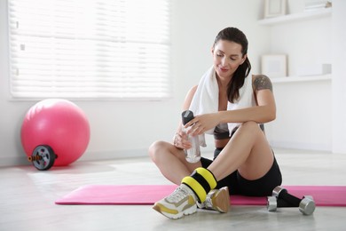 Beautiful woman with ankle weights and bottle of water indoors