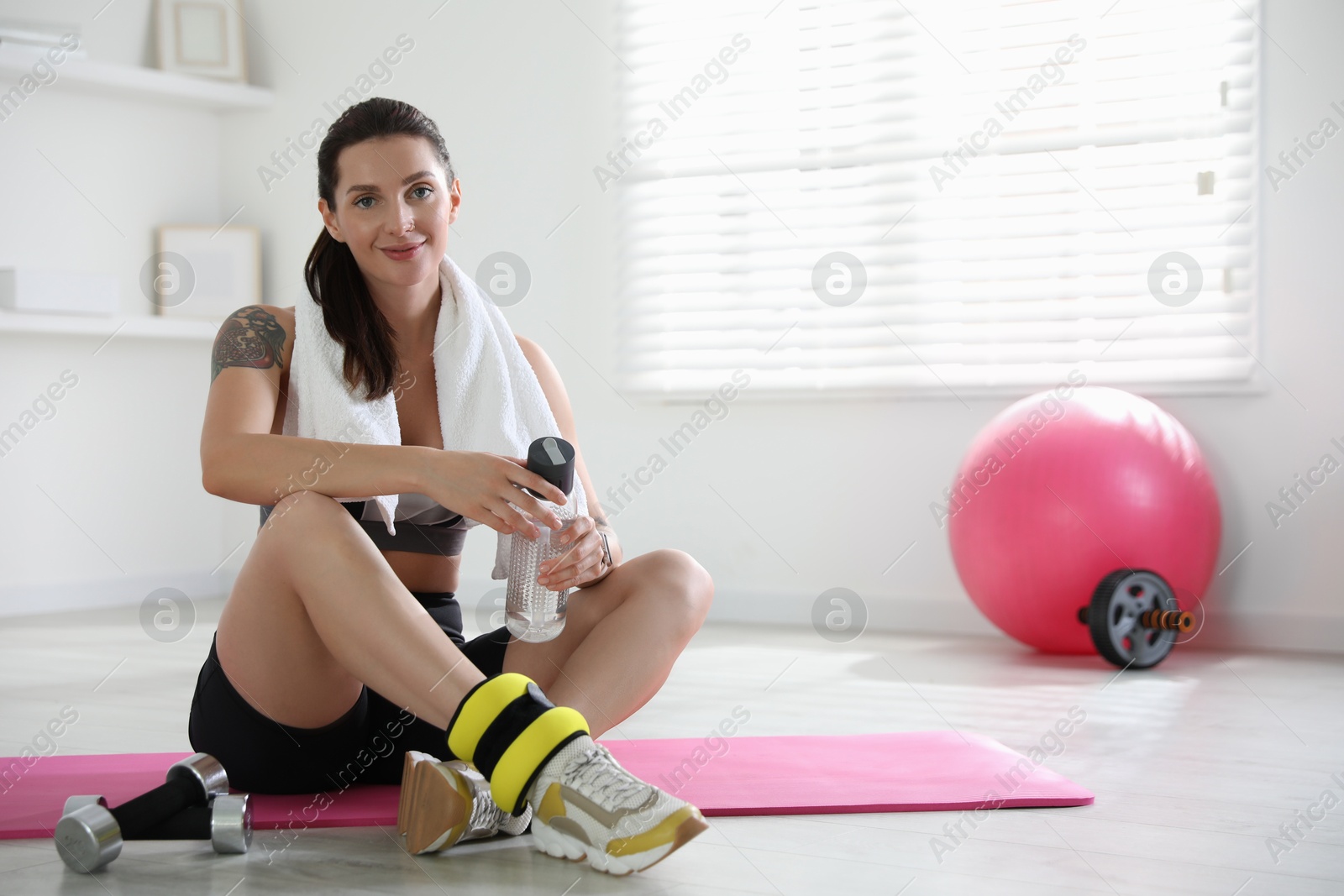 Photo of Beautiful woman with ankle weights and bottle of water indoors