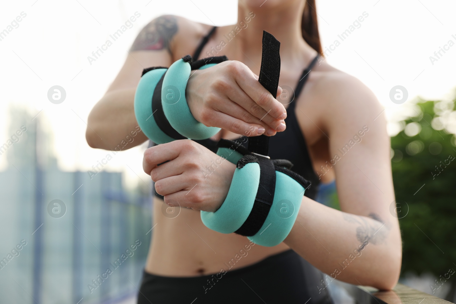 Photo of Woman putting ankle weight on her arm outdoors, closeup