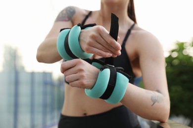 Woman putting ankle weight on her arm outdoors, closeup