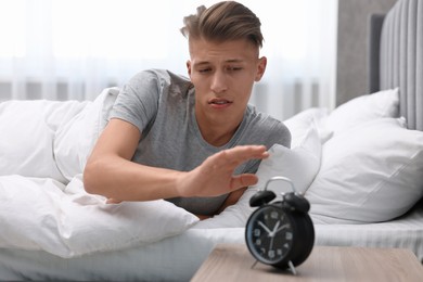 Photo of Sleepy young man turning off alarm clock in bedroom at lunch time