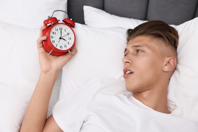 Sleepy young man in bed with alarm clock waking up at lunch time