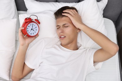 Photo of Sleepy young man in bed with alarm clock waking up at lunch time, top view