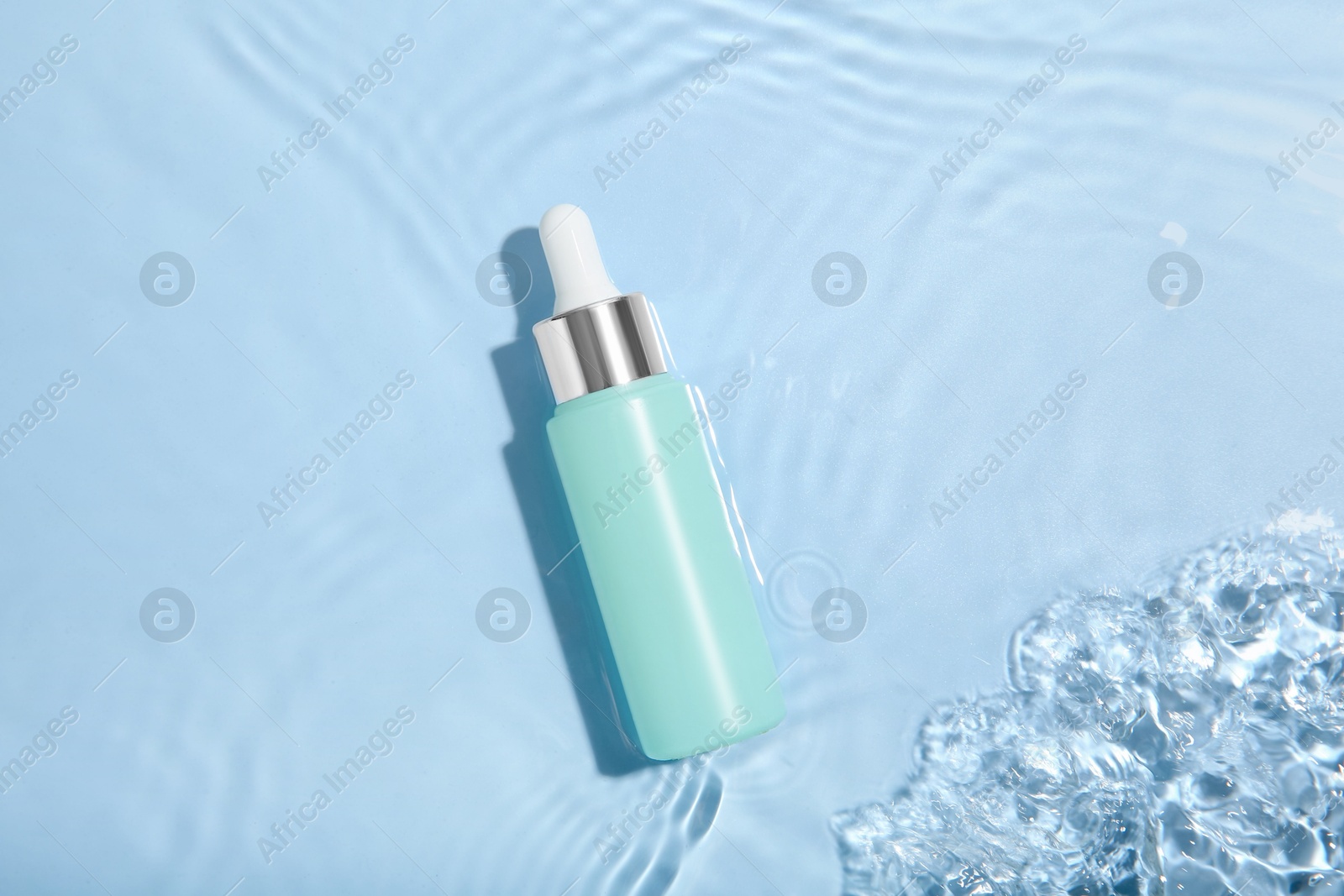 Photo of Bottle of cosmetic product in water on light blue background, top view