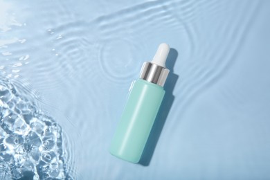 Photo of Bottle of cosmetic product in water on light blue background, top view