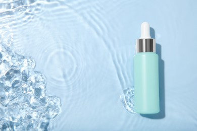 Photo of Bottle of cosmetic product in water on light blue background, top view. Space for text