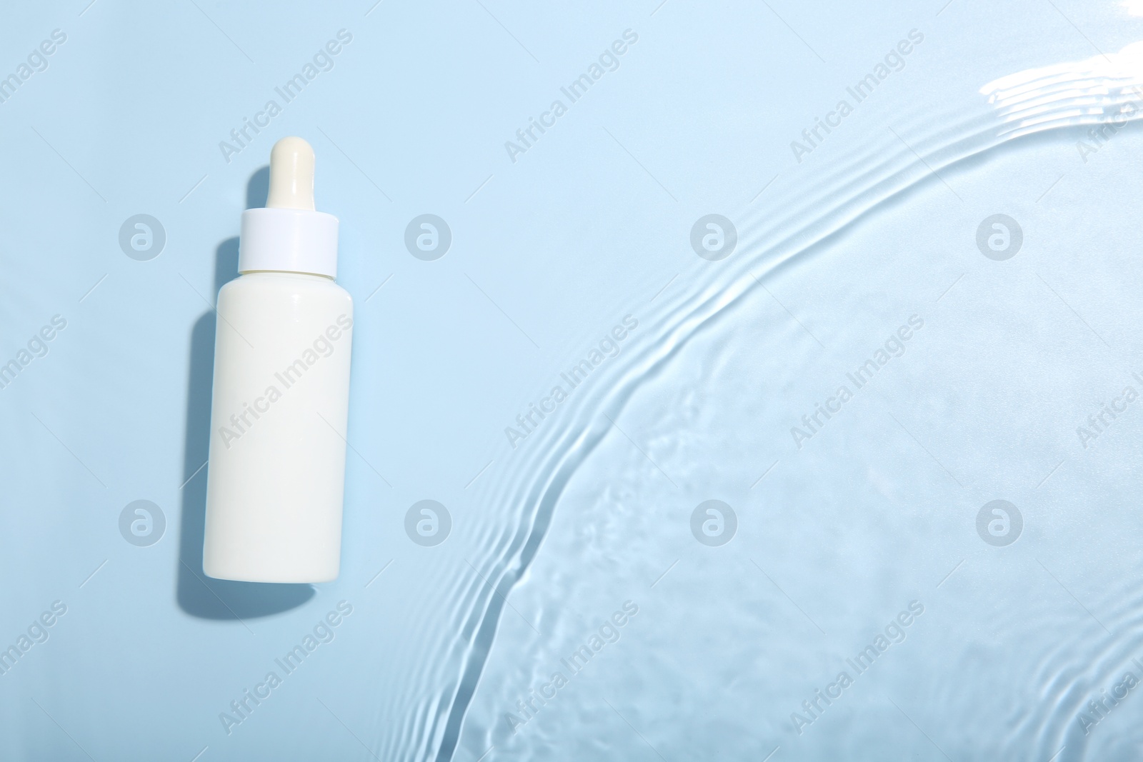 Photo of Bottle of cosmetic product in water on light blue background, top view. Space for text