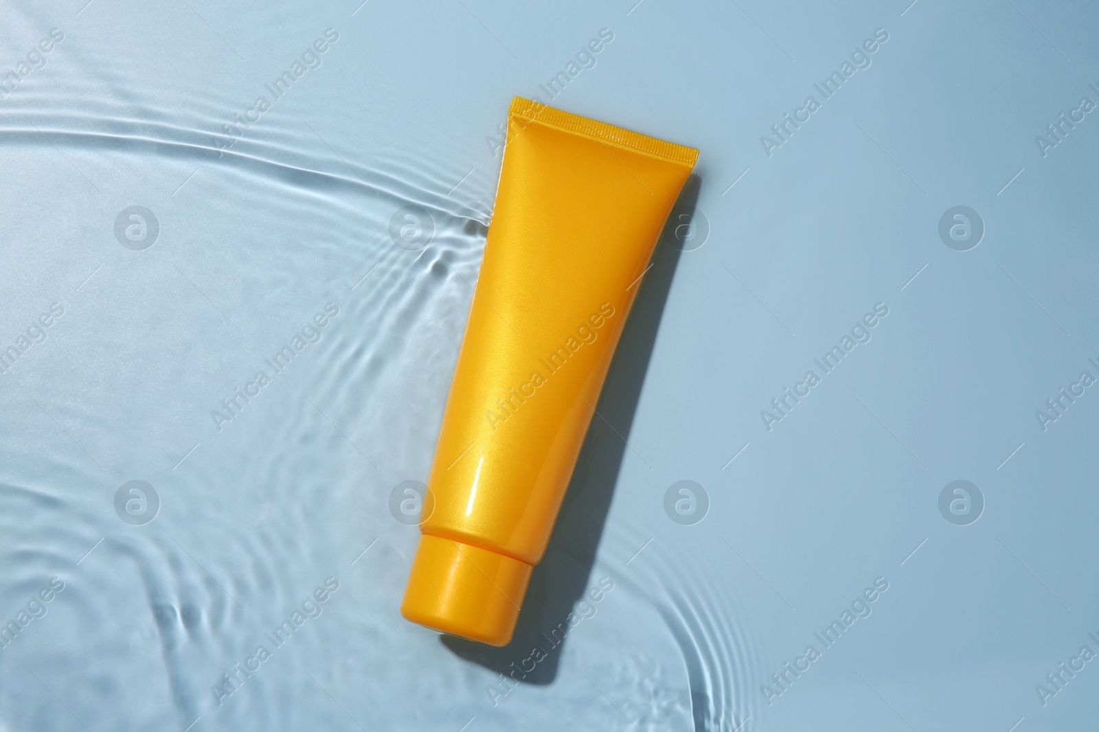 Photo of Cosmetic product. Tube with cream in water on light blue background, top view