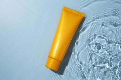 Photo of Cosmetic product. Tube with cream in water on light blue background, top view