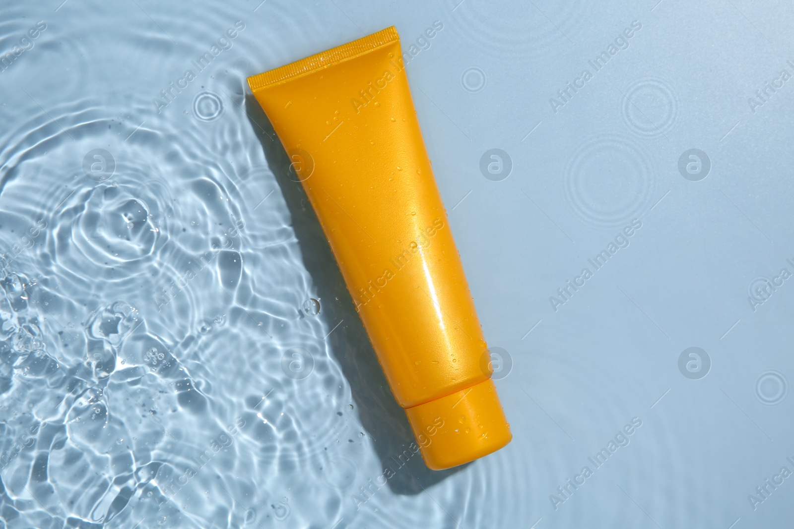 Photo of Cosmetic product. Tube with cream in water on light blue background, top view