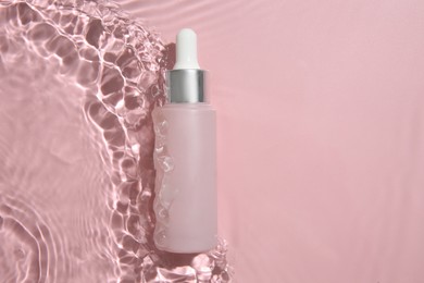 Photo of Bottle of cosmetic product in water on pink background, top view. Space for text