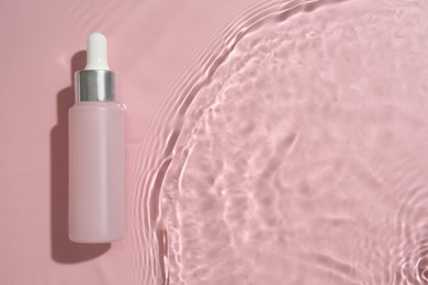 Photo of Bottle of cosmetic product in water on pink background, top view. Space for text