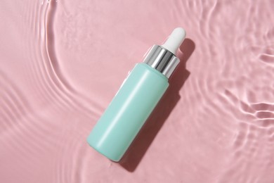 Photo of Bottle of cosmetic product in water on pink background, top view