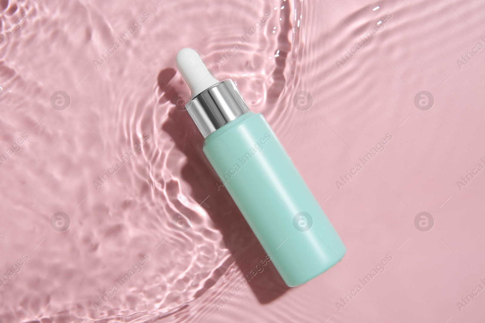 Photo of Bottle of cosmetic product in water on pink background, top view