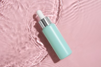 Photo of Bottle of cosmetic product in water on pink background, top view