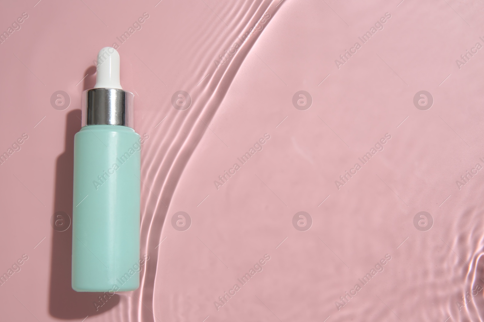 Photo of Bottle of cosmetic product in water on pink background, top view. Space for text