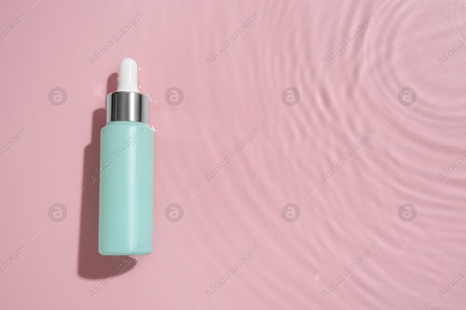 Photo of Bottle of cosmetic product in water on pink background, top view. Space for text