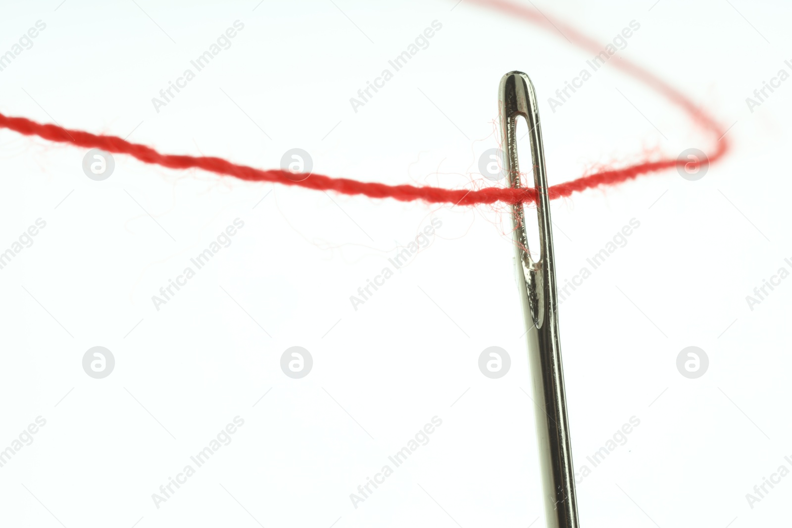 Photo of Sewing needle with red thread on white background, closeup