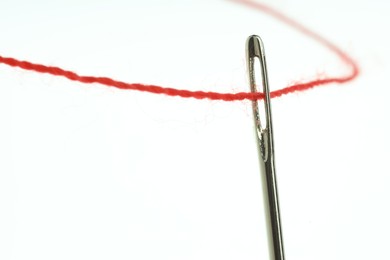 Sewing needle with red thread on white background, closeup