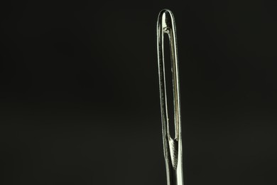 Photo of Sewing needle on black background, closeup view. Space for text