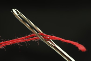 Sewing needle with red thread on black background, closeup