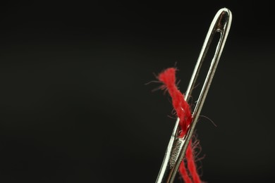 Photo of Sewing needle with red thread on black background, closeup. Space for text