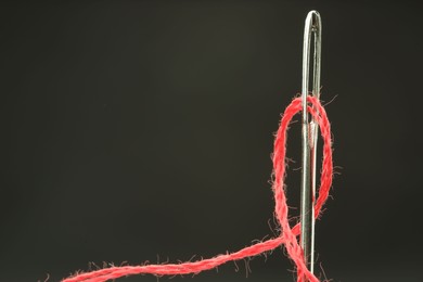 Photo of Sewing needle with red thread on black background, closeup. Space for text