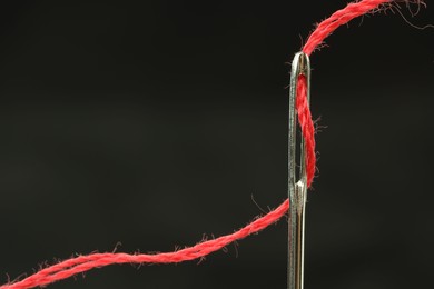 Sewing needle with red thread on black background, closeup. Space for text