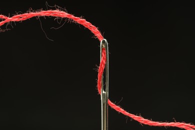 Photo of Sewing needle with red thread on black background, closeup