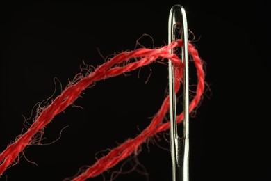 Photo of Sewing needle with red thread on black background, closeup