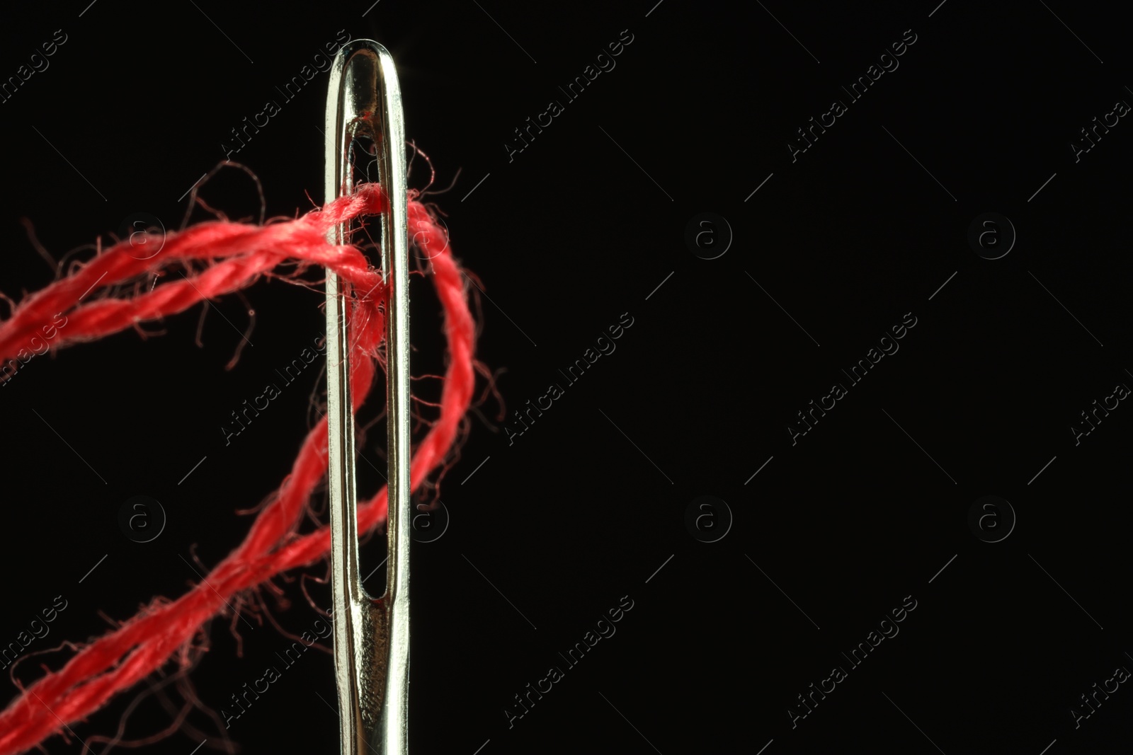 Photo of Sewing needle with red thread on black background, closeup. Space for text