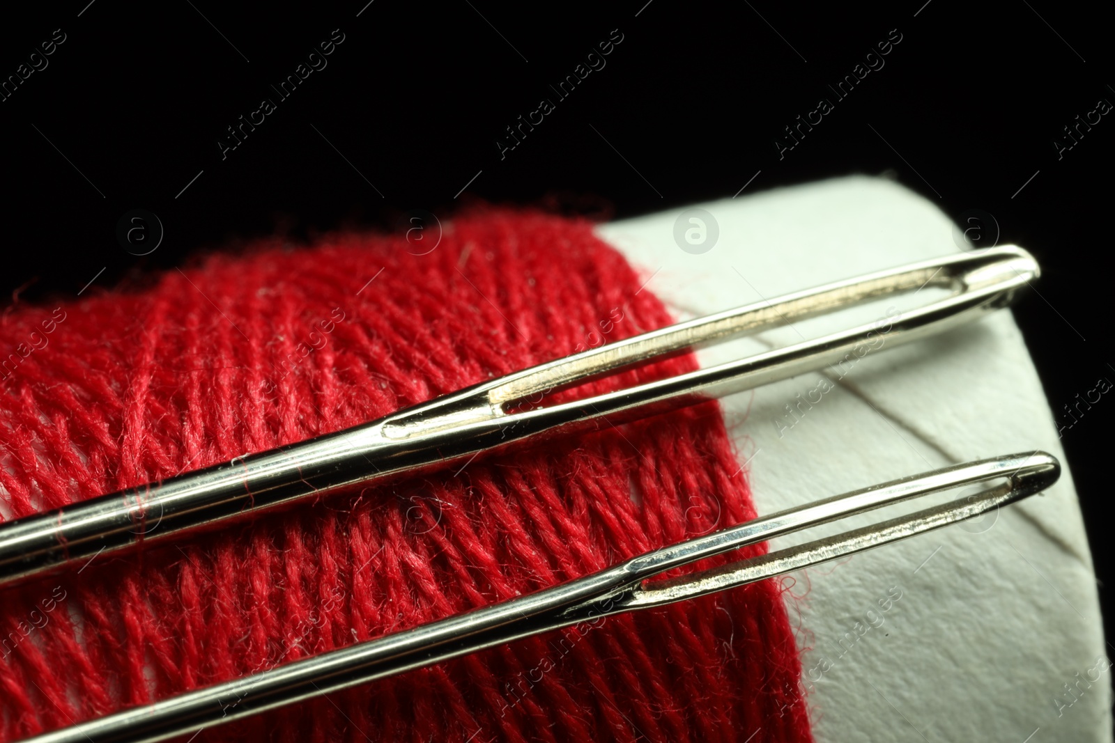 Photo of Spool of red sewing thread with needles on black background, closeup