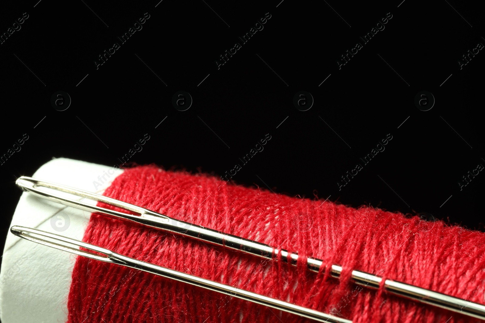 Photo of Spool of red sewing thread with needles on black background, closeup