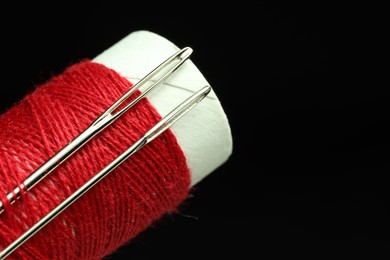 Photo of Spool of red sewing thread with needles on black background, closeup. Space for text