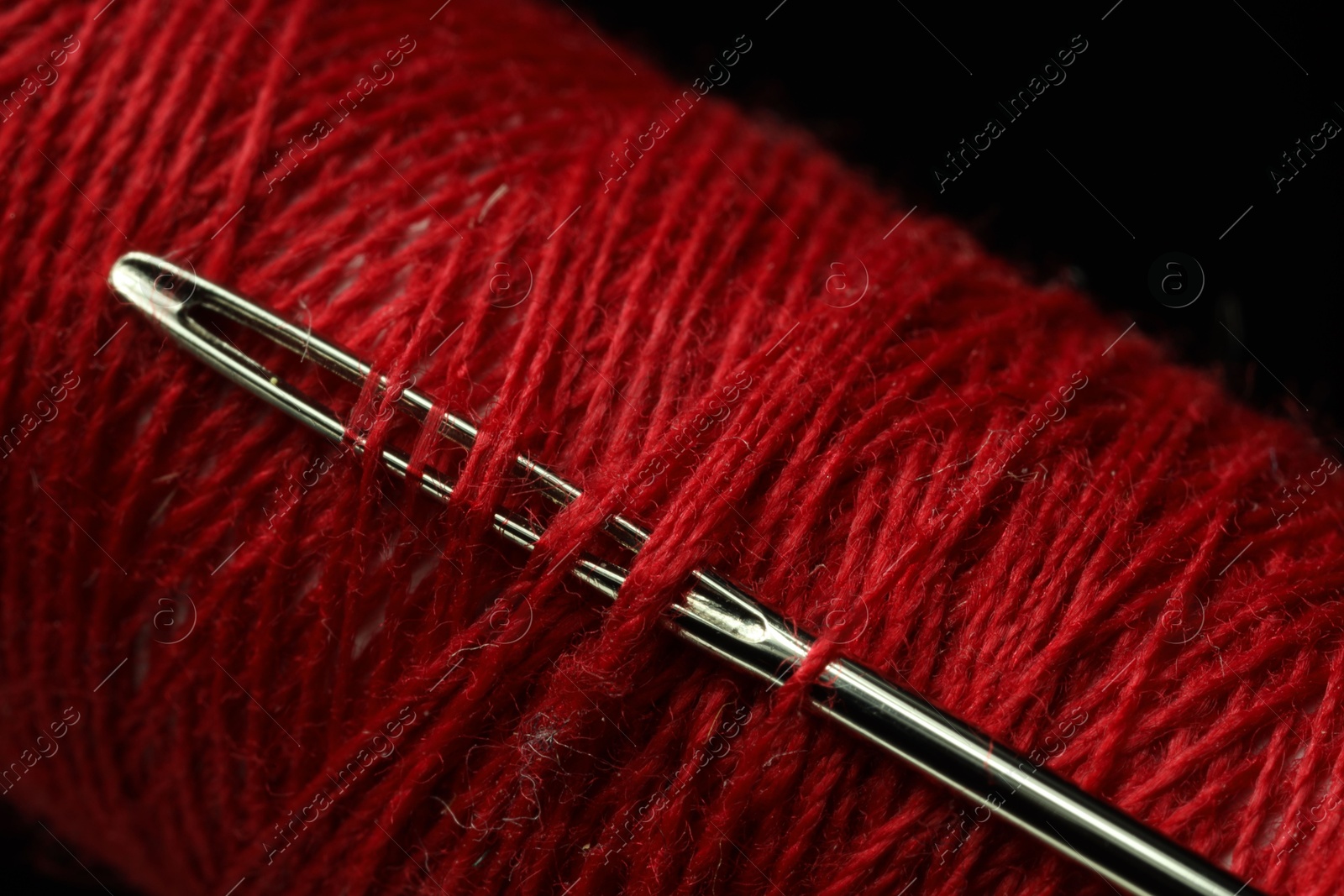 Photo of Spool of red sewing thread with needle on black background, closeup