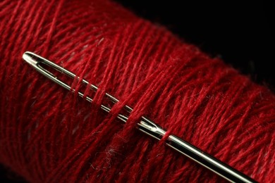 Photo of Spool of red sewing thread with needle on black background, closeup