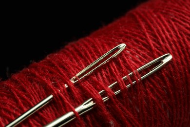 Photo of Spool of red sewing thread with needles on black background, closeup