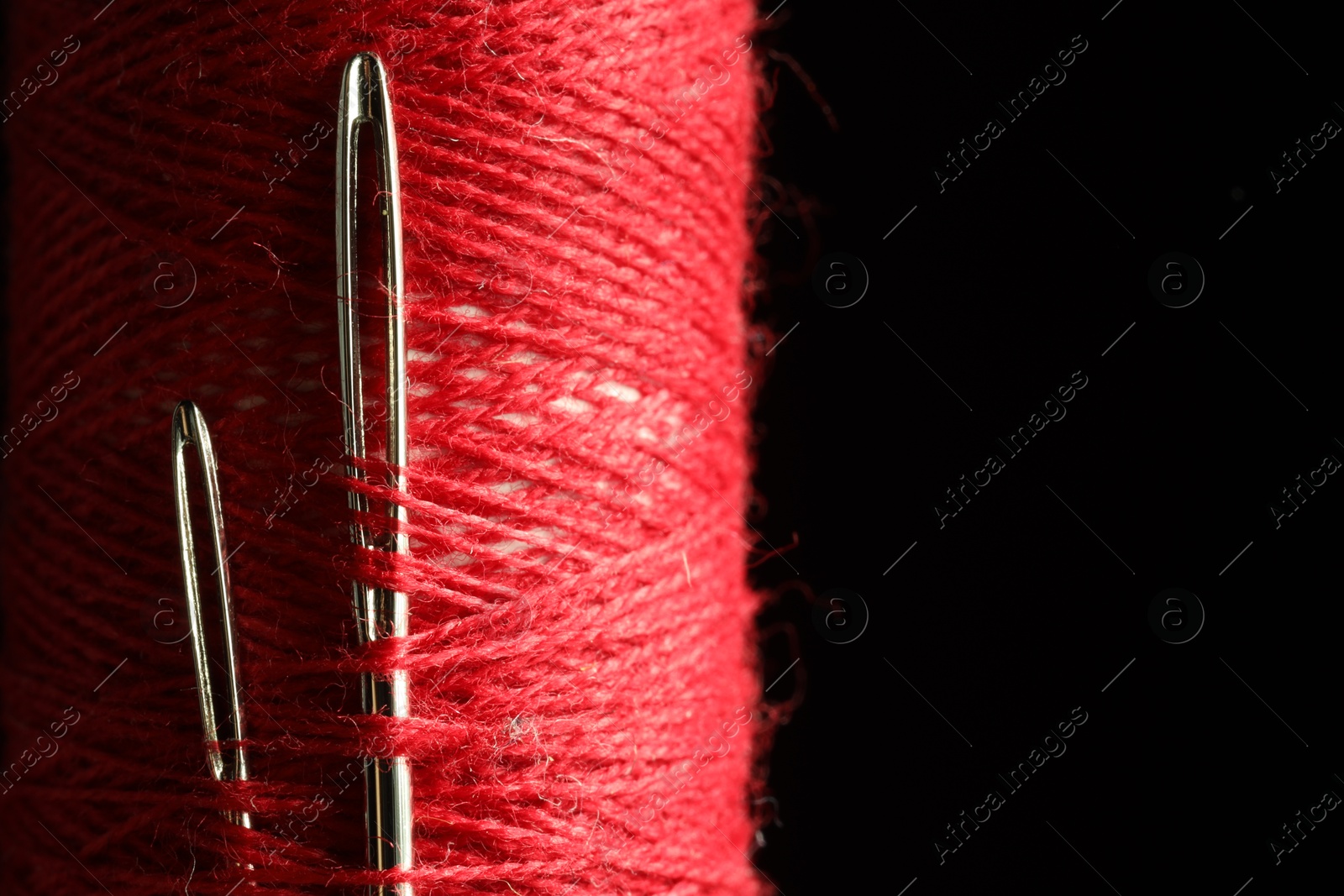 Photo of Spool of red sewing thread with needles on black background, closeup. Space for text