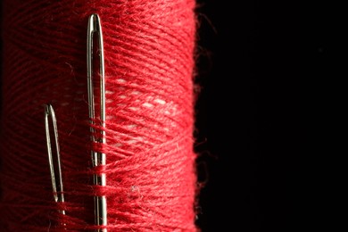 Spool of red sewing thread with needles on black background, closeup. Space for text