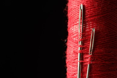 Photo of Spool of red sewing thread with needles on black background, closeup. Space for text