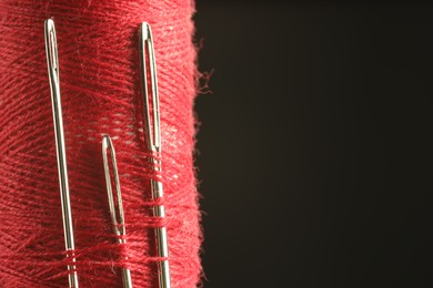 Photo of Spool of red sewing thread with needles on black background, closeup. Space for text