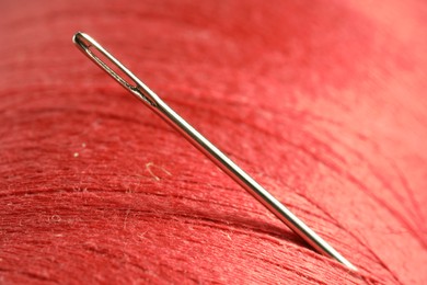 Spool of red sewing thread with needle, macro view