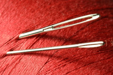 Photo of Spool of red sewing thread with needles, macro view