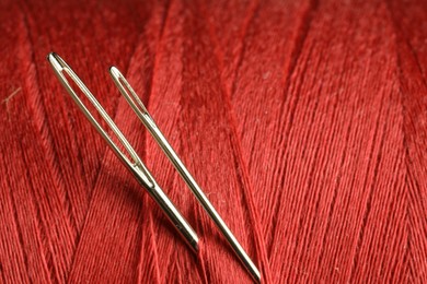 Spool of red sewing thread with needles, macro view