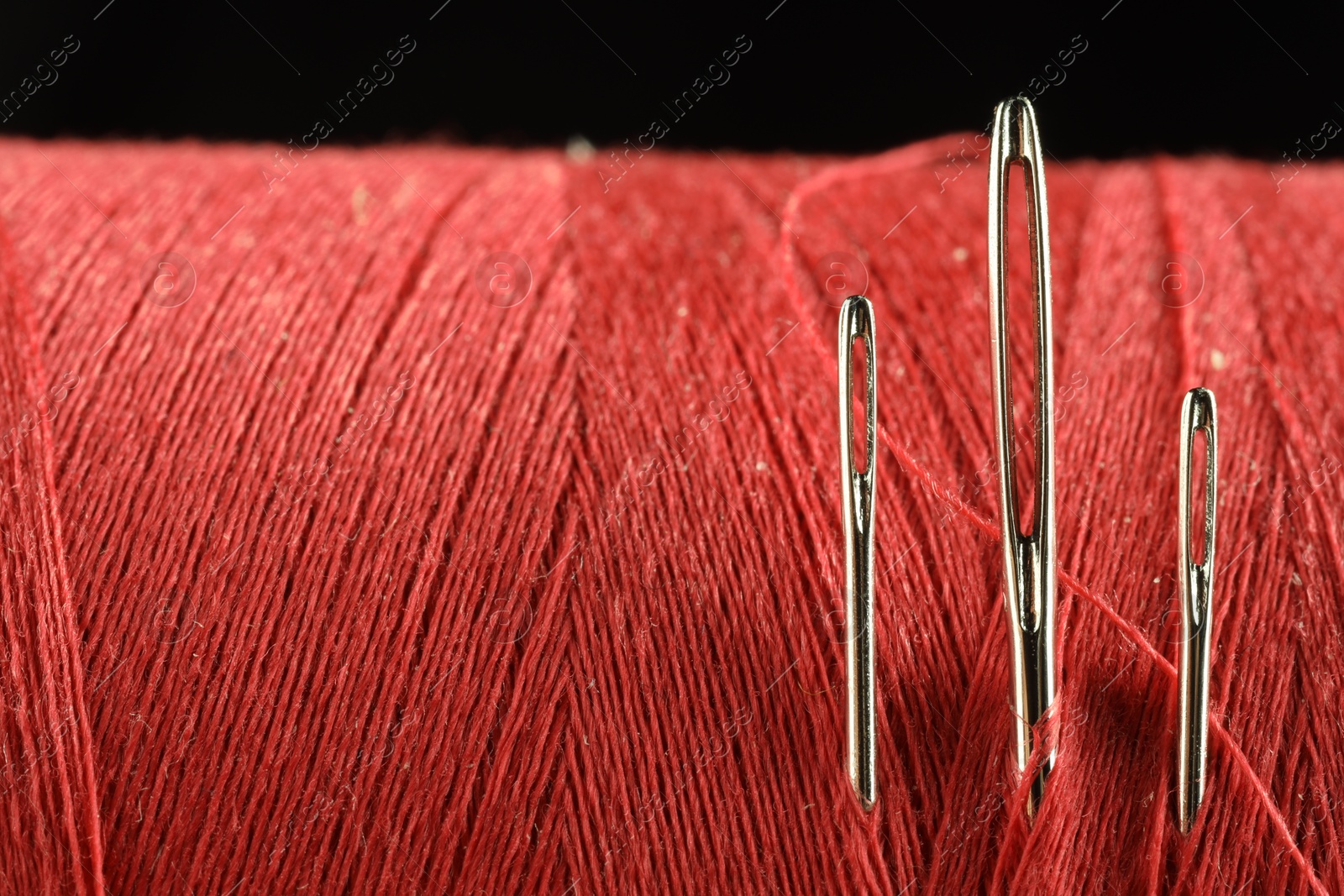 Photo of Spool of red sewing thread with needles on black background, macro view